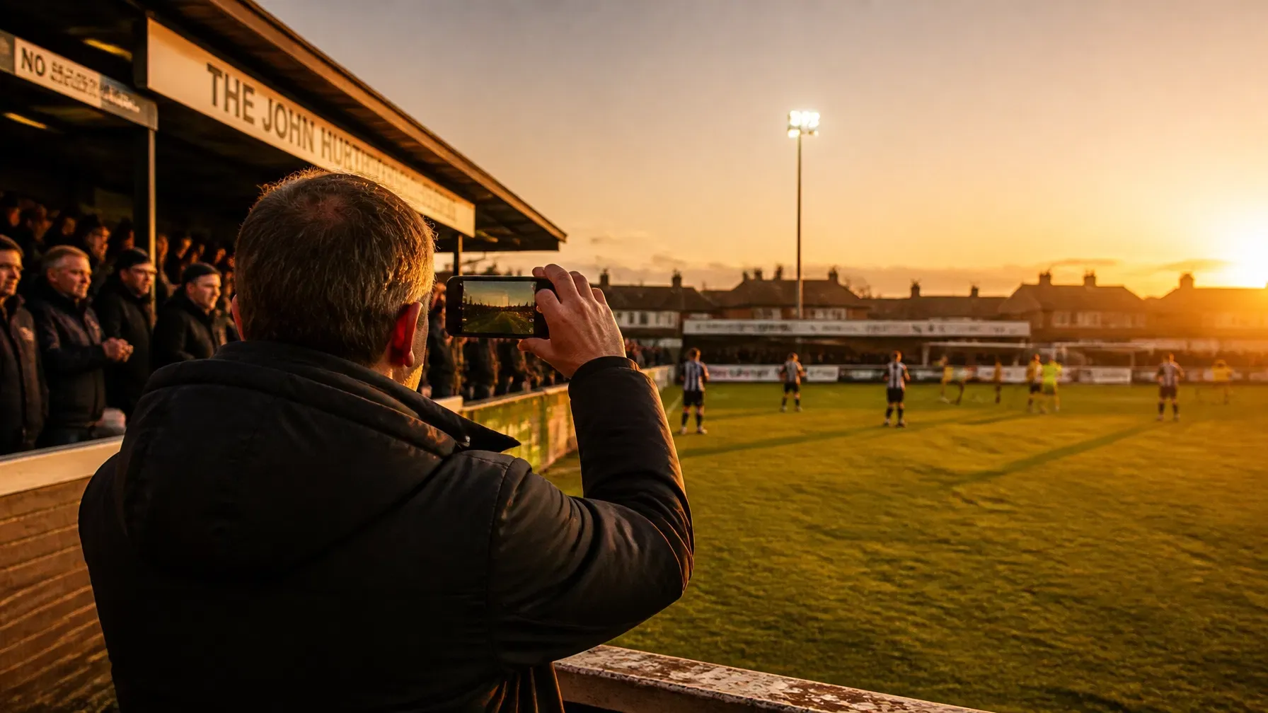 Supporter filming a floodlit match from the terrace